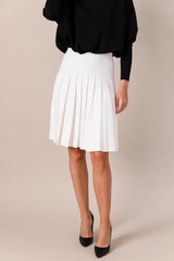 Person wearing a black top and white pleated skirt on a beige background