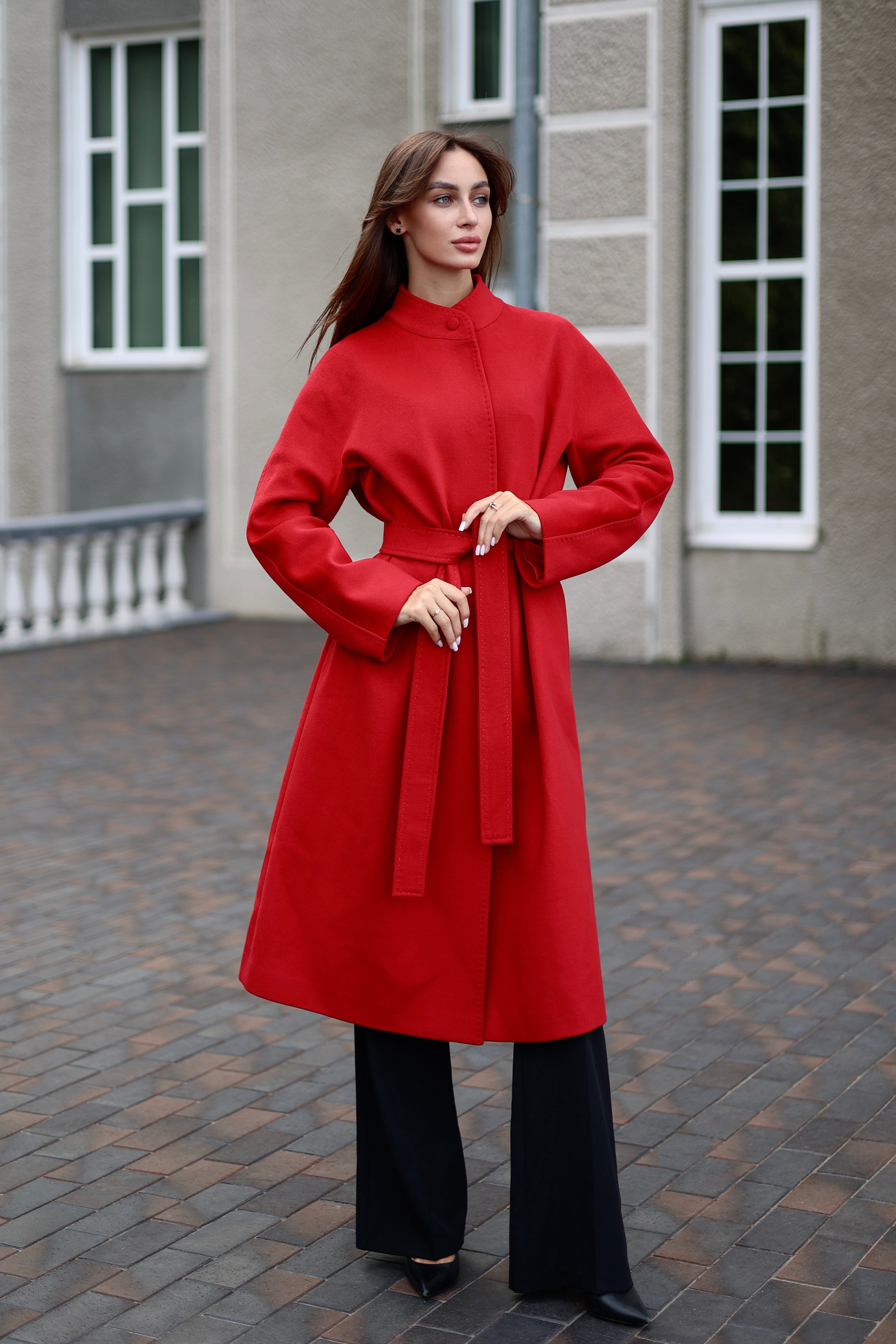 Woman wearing a red coat standing on a paved area with a building in the background