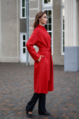 Woman wearing a red coat standing on a paved area with a building in the background