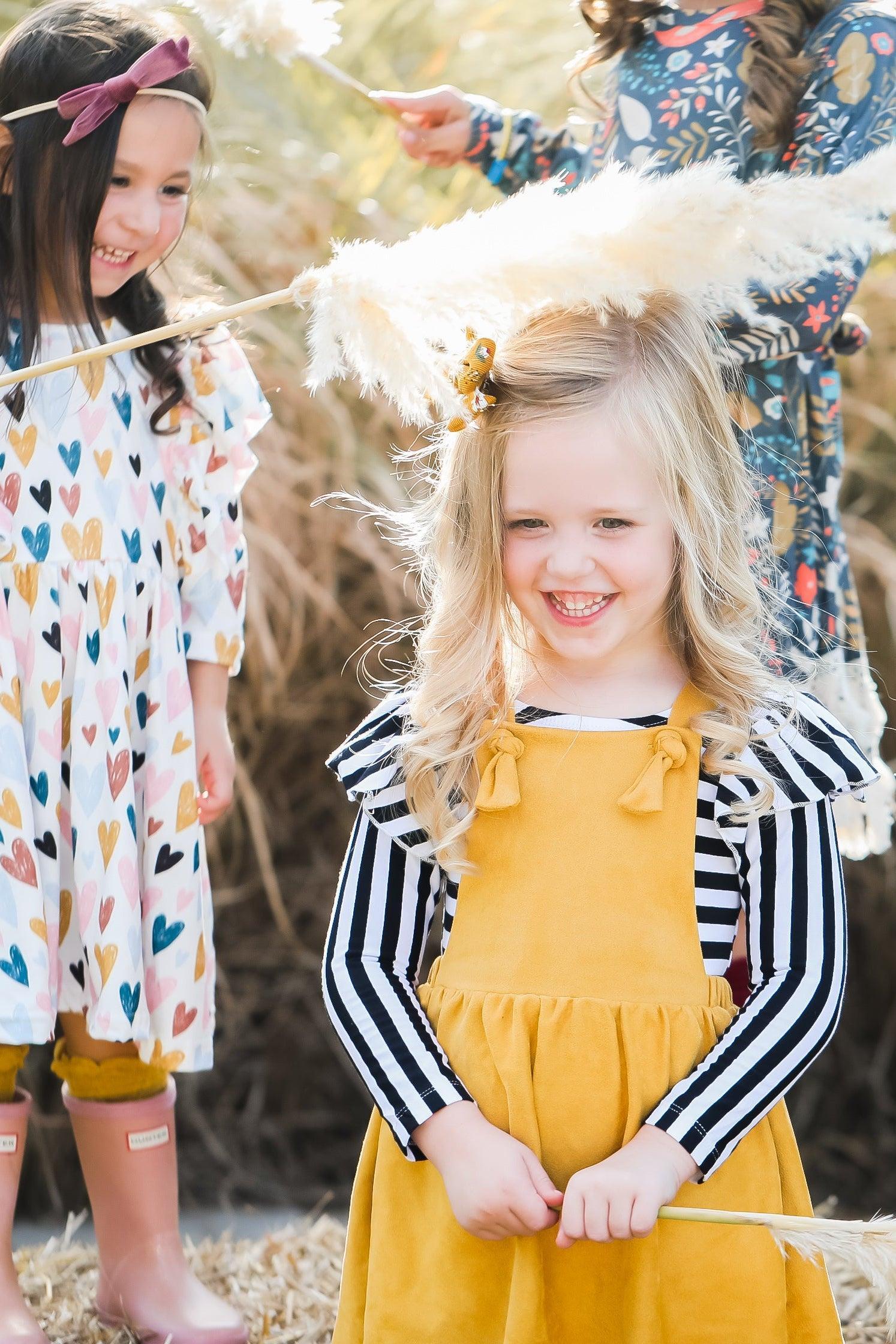 Two young girls in colorful outfits standing outdoors with straw decorations.