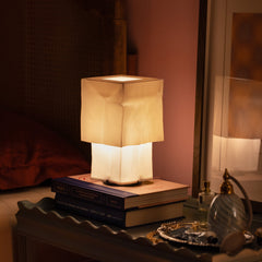 Table lamp with a soft glow on top of books in a dimly lit room.