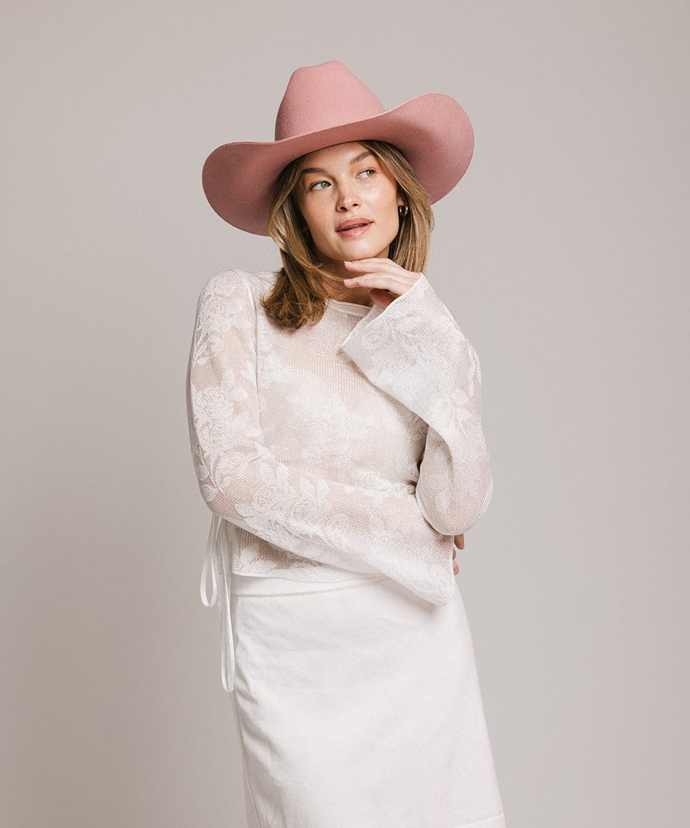 Woman wearing a pink wide-brimmed hat and white outfit against a plain background