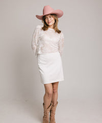 Person wearing a white outfit with a pink hat and brown boots on a plain background