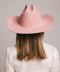 Person wearing a pink cowboy hat with a gold emblem on a plain background