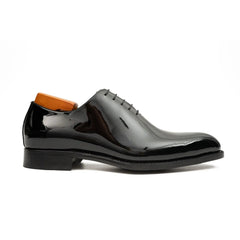 Black patent leather shoe with orange lining on a white background