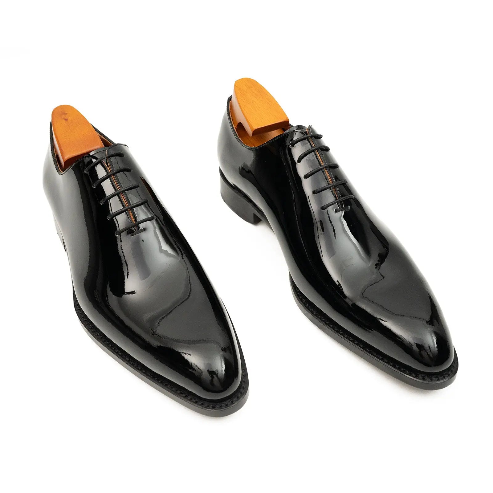Pair of black patent leather shoes with orange tips on a white background