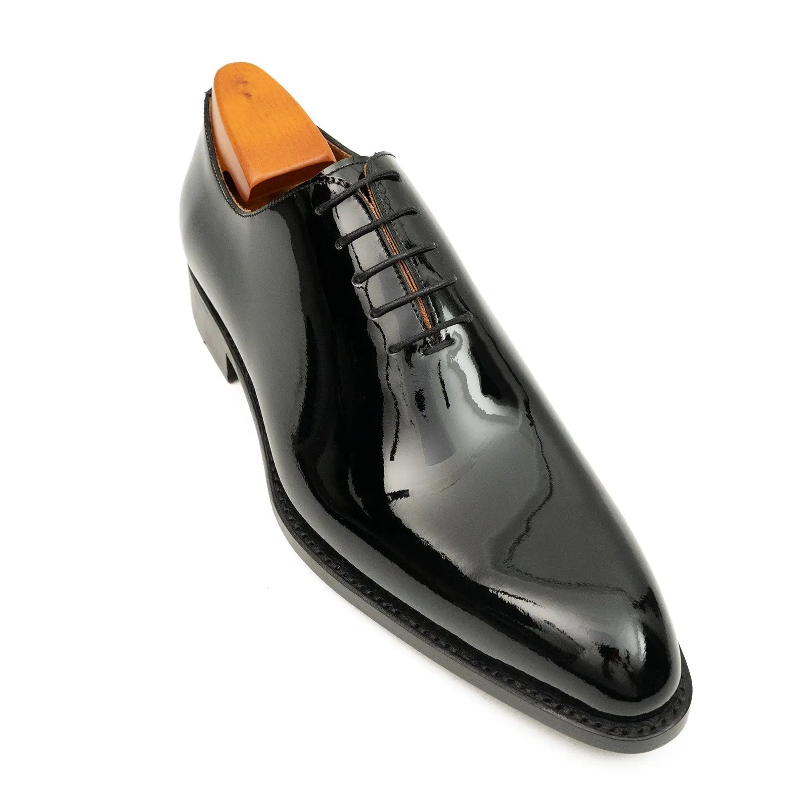 Shiny black dress shoe with orange heel on a white background