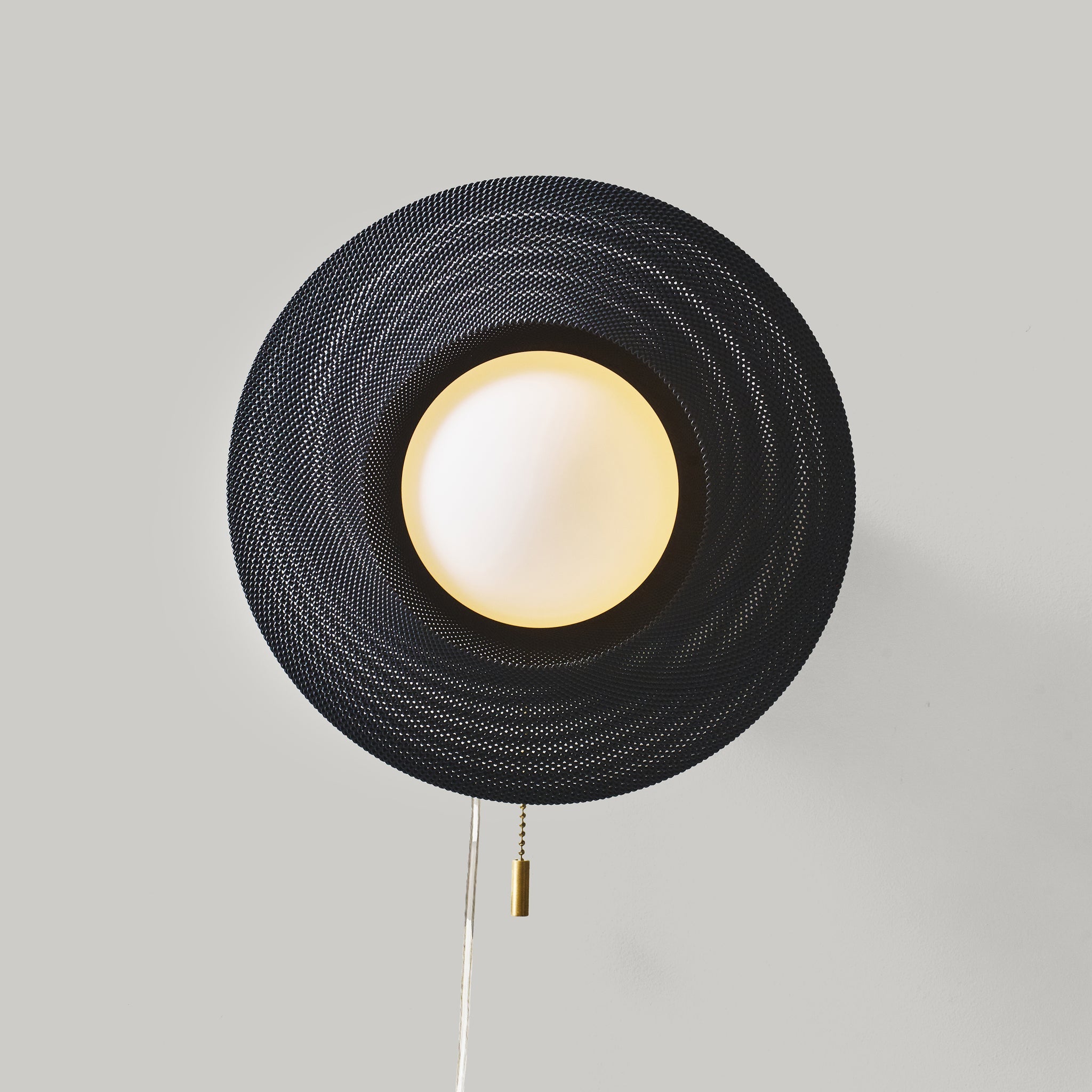 Wall-mounted lamp with black woven shade and white bulb on a gray background