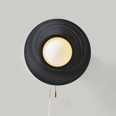 Wall-mounted lamp with black woven shade and white bulb on a gray background