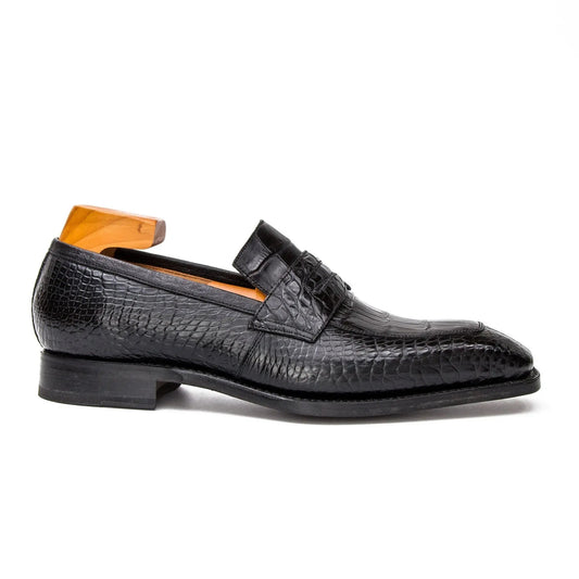 A single black crocodile-embossed leather loafer shown in profile on a white background, with a wooden shoe tree insert visible inside.