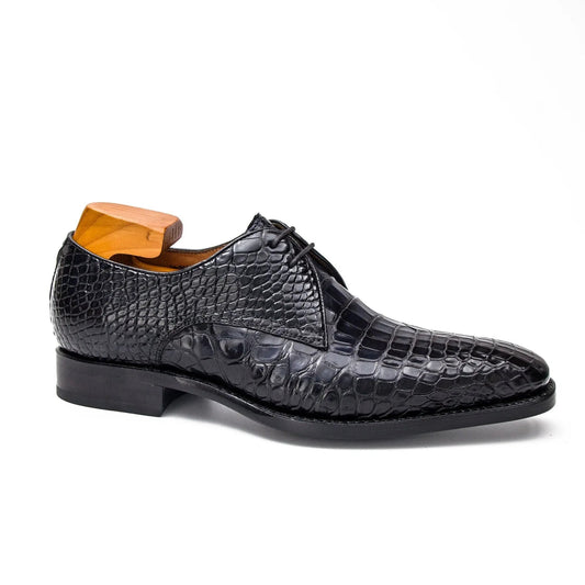 A black crocodile-embossed leather oxford dress shoe with a wooden shoe tree inserted, shown in a side profile on a white background.