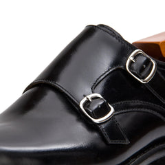 Close-up of a black leather shoe with silver buckles on a white background