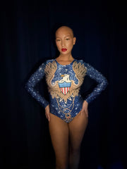 Person wearing a blue and gold leotard with an eagle emblem on a black background