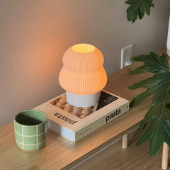 Small orange lamp on a box with 'pasta' text, next to a green mug and plant on a wooden surface.