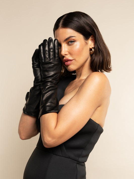 Woman wearing black leather gloves and a black dress against a beige background