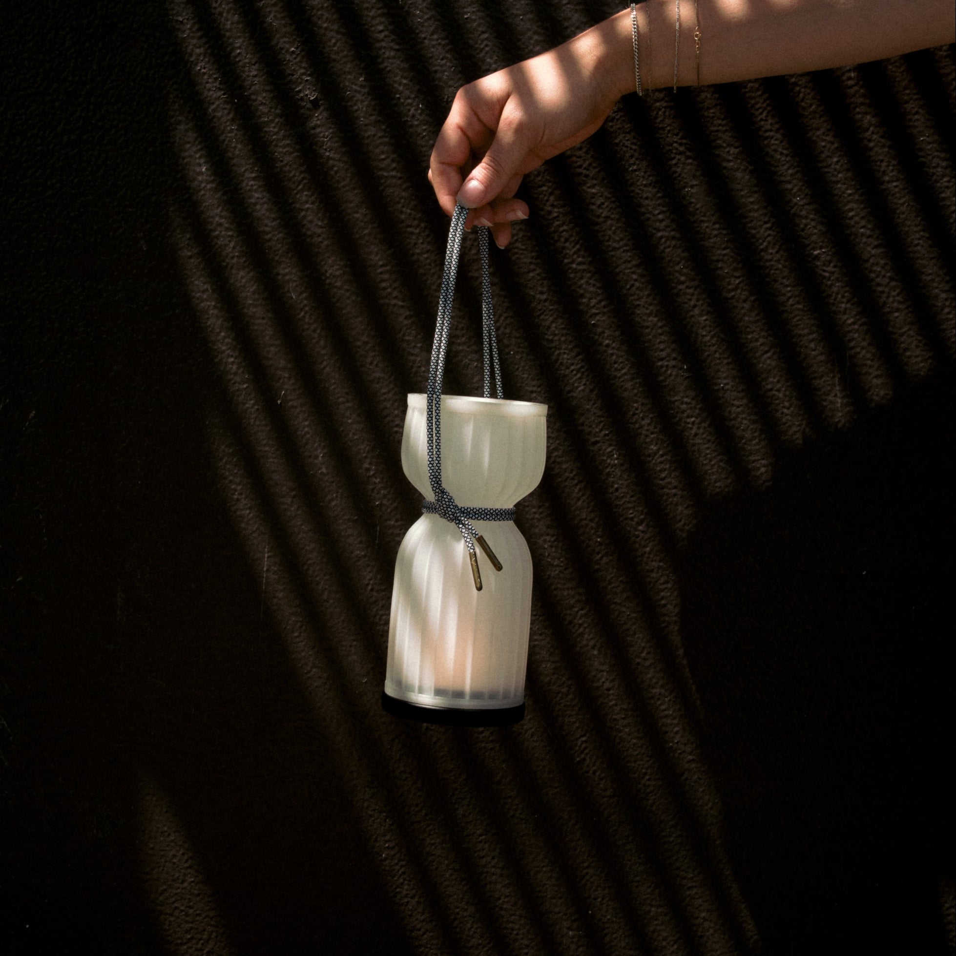 White ceramic lantern held by a hand against a dark textured background
