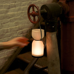 Vintage-style lamp attached to a pipe with a hand reaching towards it against a brick wall.