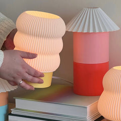 Person adjusting a textured lamp on a stack of books with other colorful lamps in the background.