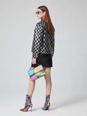 Woman in a checkered shirt and black skirt holding a colorful clutch against a white background