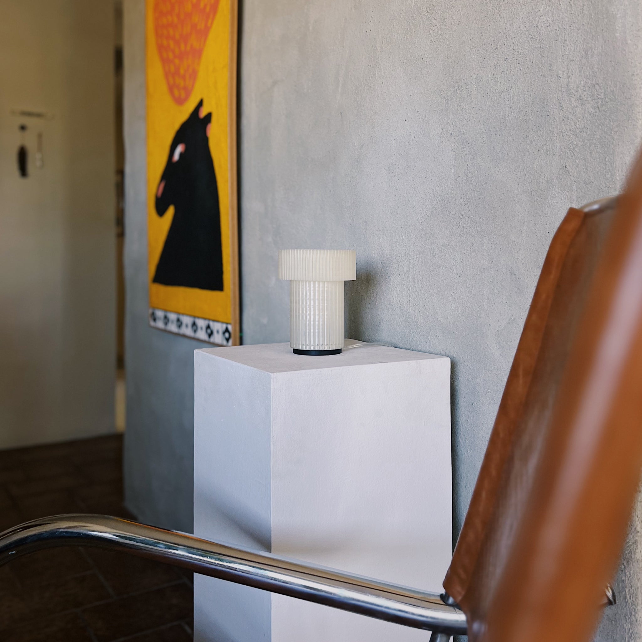 White cylindrical object on a stand with a horse painting in the background