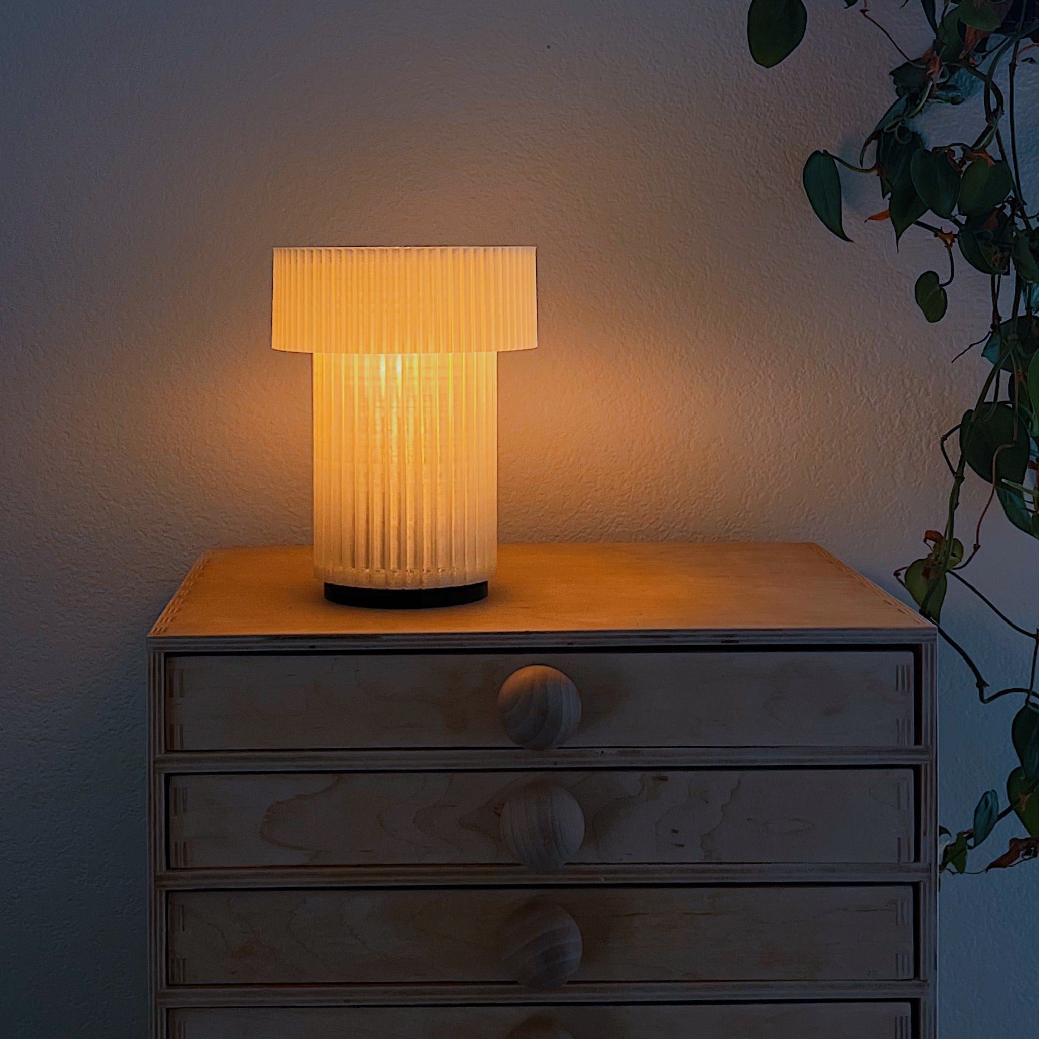 Table lamp with a ribbed design on a wooden surface next to a plant