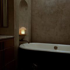 Bathroom with a bathtub and a lit lamp on a shelf.