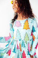 A young girl wearing a light blue long-sleeve dress with a colorful Christmas tree print, shown in a close-up profile view against a plain white background.