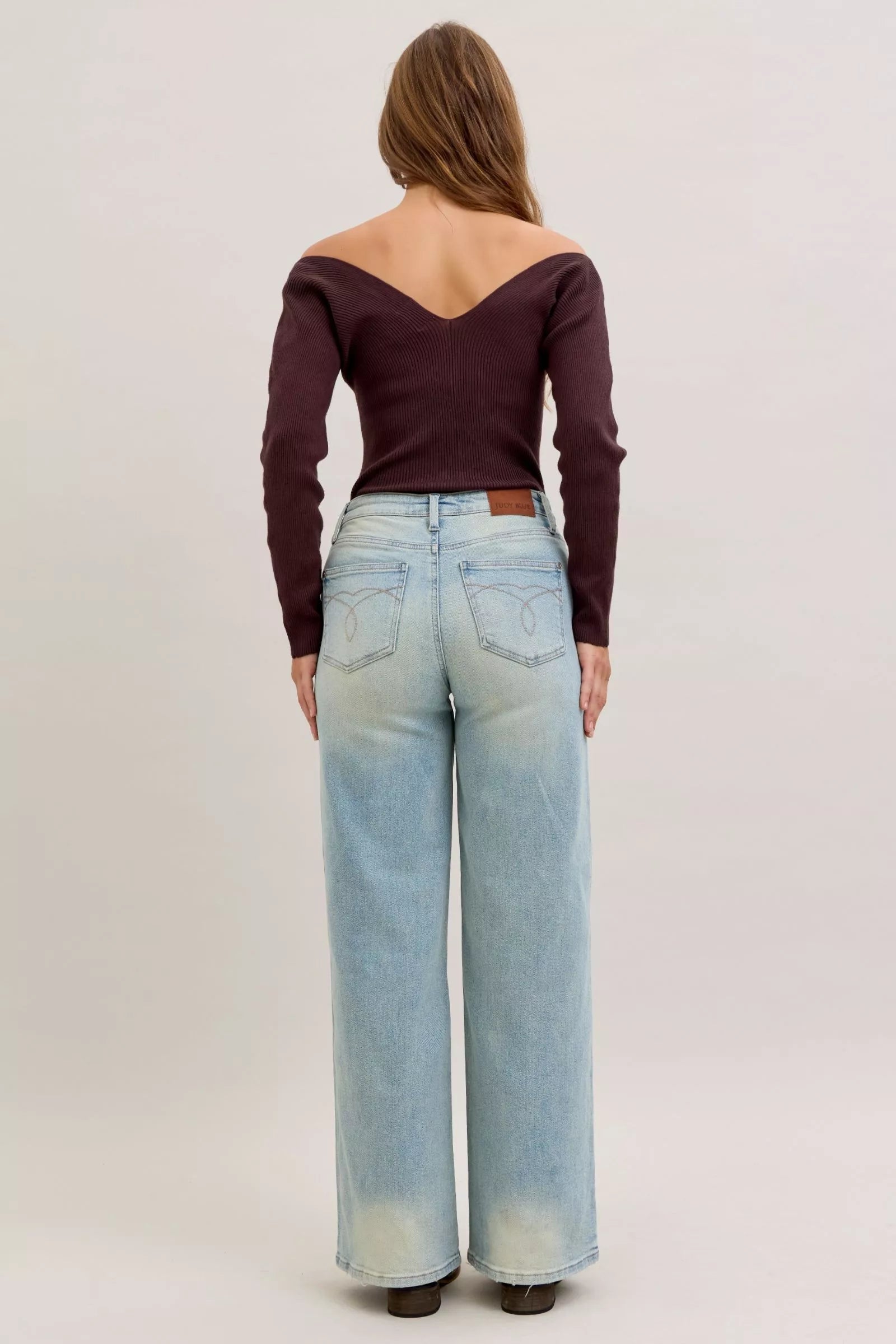 Person wearing a burgundy off-shoulder top and light blue jeans on a plain background