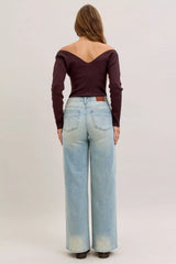 Person wearing a burgundy off-shoulder top and light blue jeans on a plain background