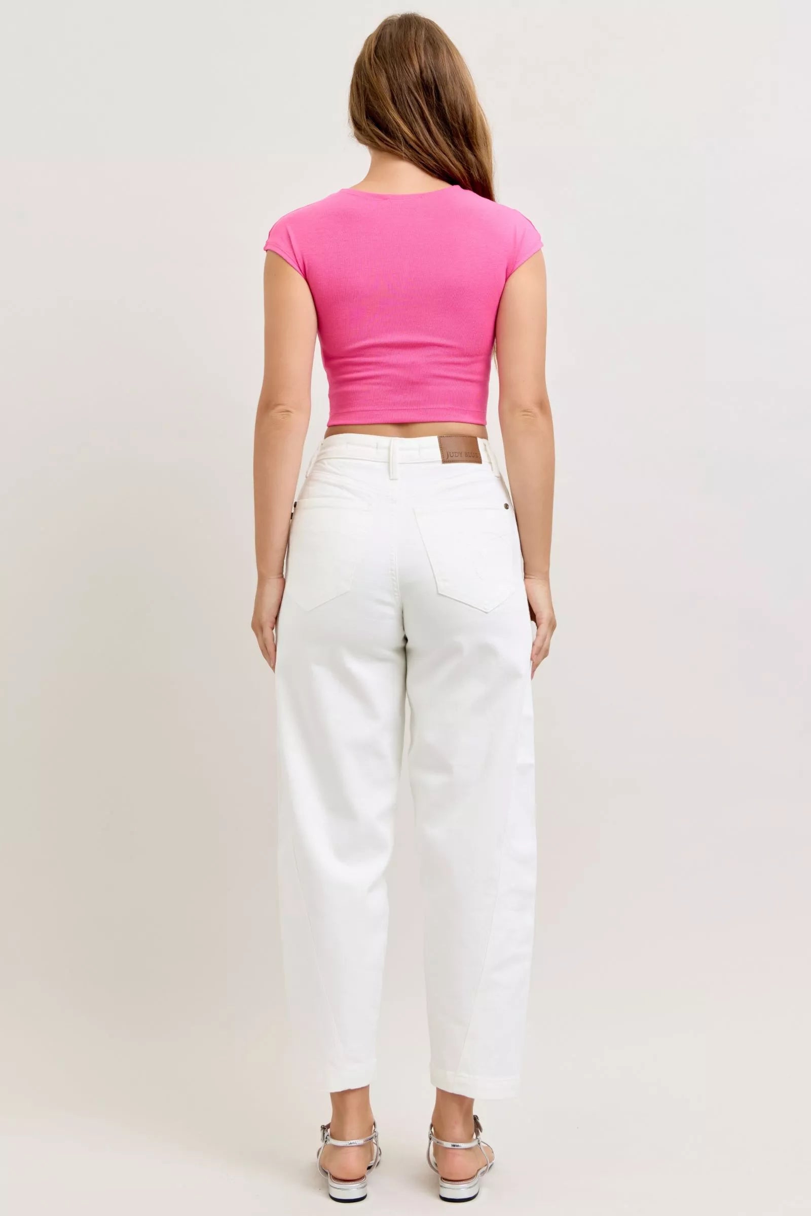 Person wearing a pink top and white pants on a plain background