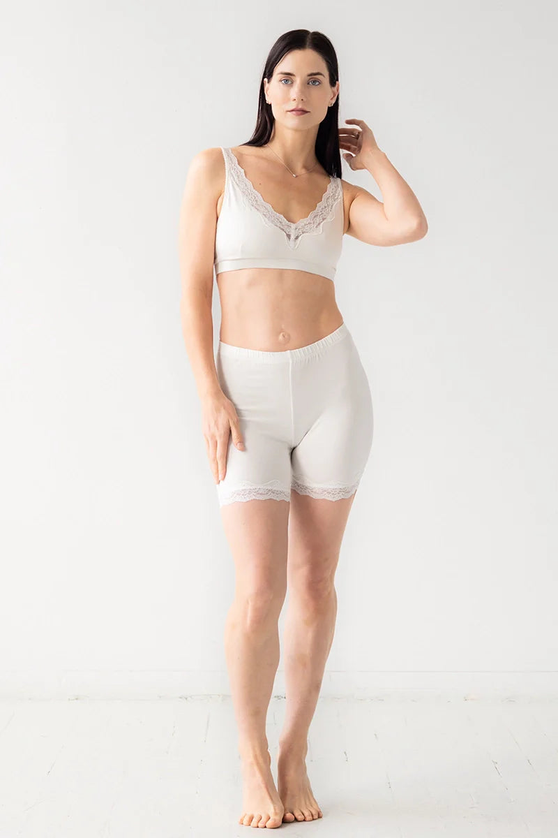 Woman wearing a white lace bralette and high-waisted shorts on a light gray background