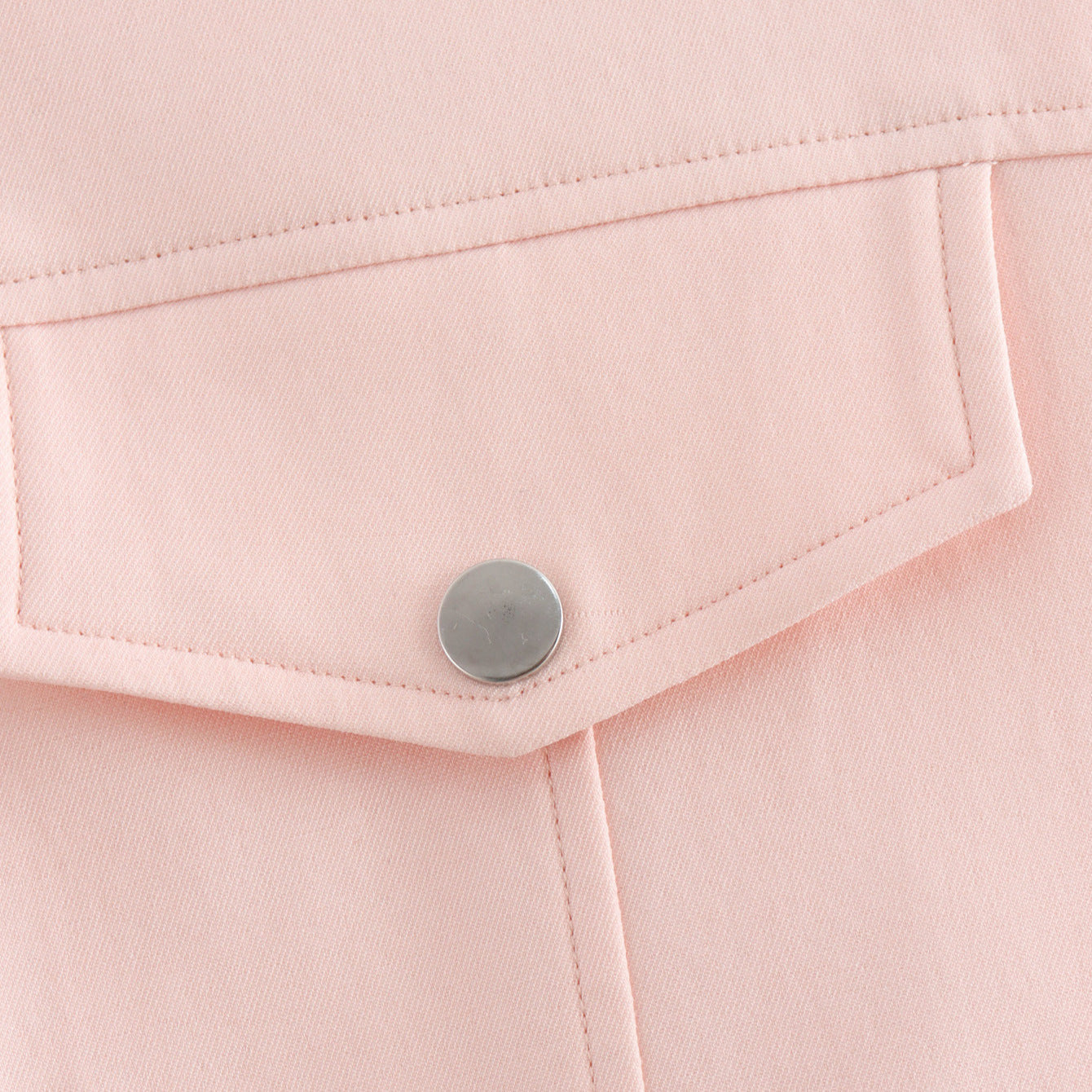 Close-up of a pink fabric pocket with a button on a light pink background