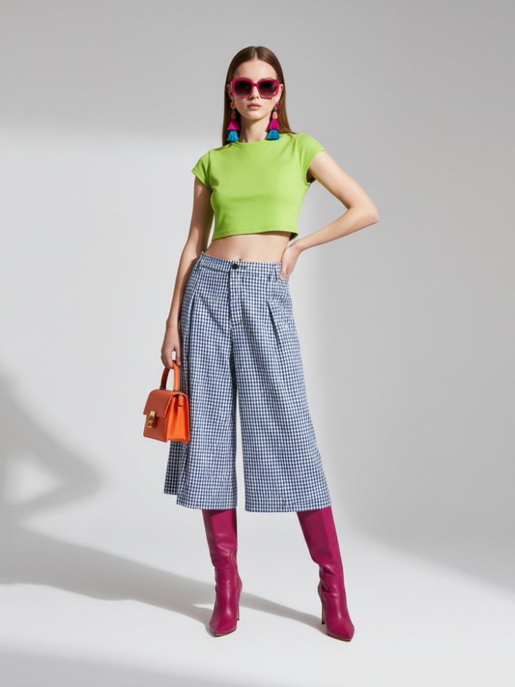 Woman wearing a green top, blue checkered pants, and pink boots on a gray background