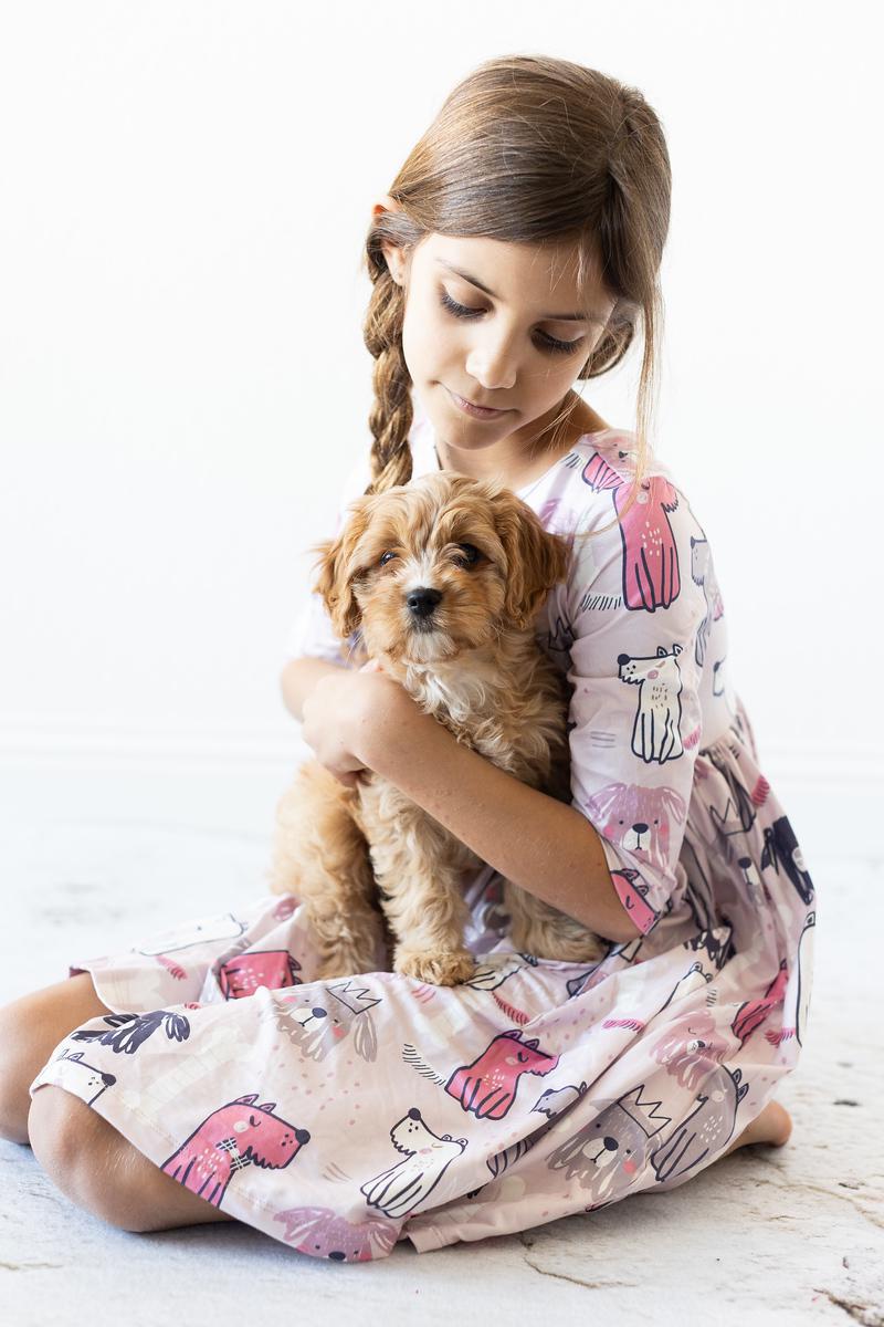 Girl in a patterned dress holding a small dog on a light background