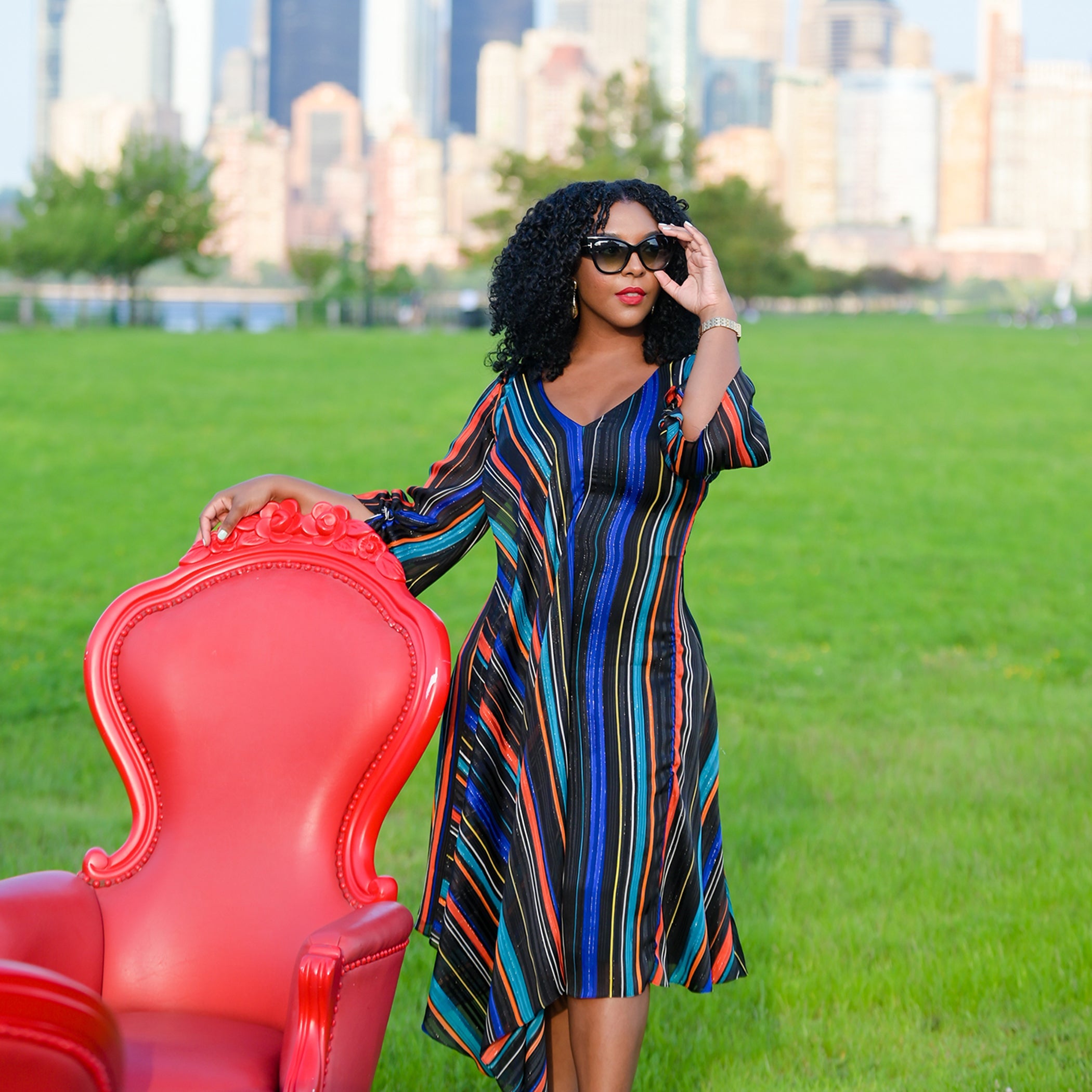 Woman in a colorful dress holding a red chair with a cityscape in the background