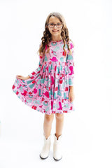 Young girl wearing a colorful dress with a pattern of boots and flowers on a white background