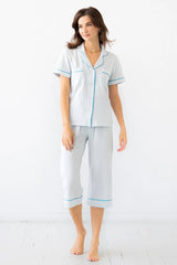 Woman wearing a light gray pajama set with blue piping on a white background