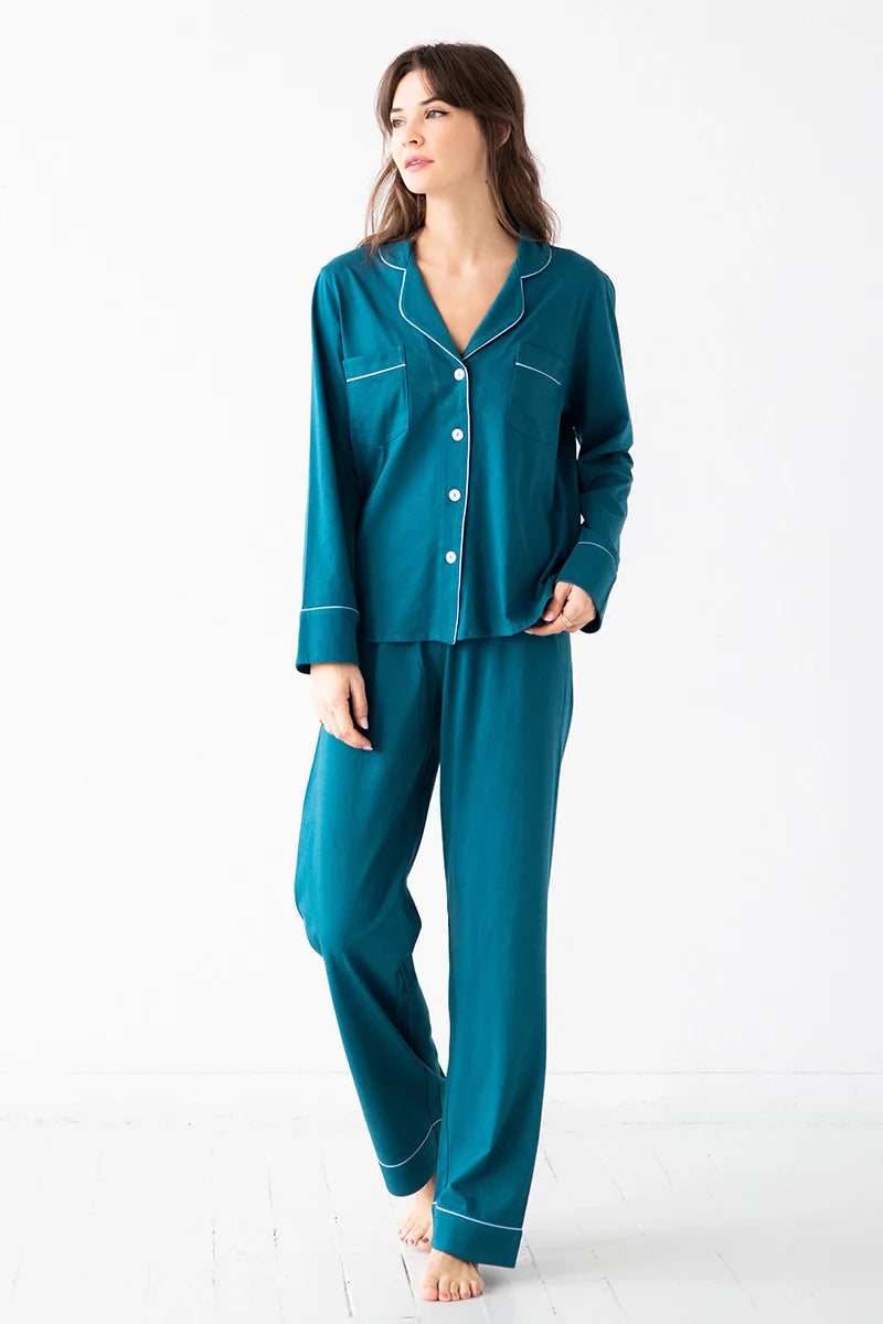 Woman wearing teal pajamas with white piping on a white background