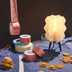 Decorative tape rolls and a lamp on a grid surface with small models.
