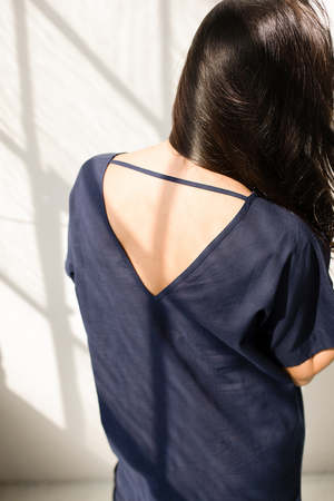 Person wearing a dark blue top with thin straps, standing in a softly lit room.