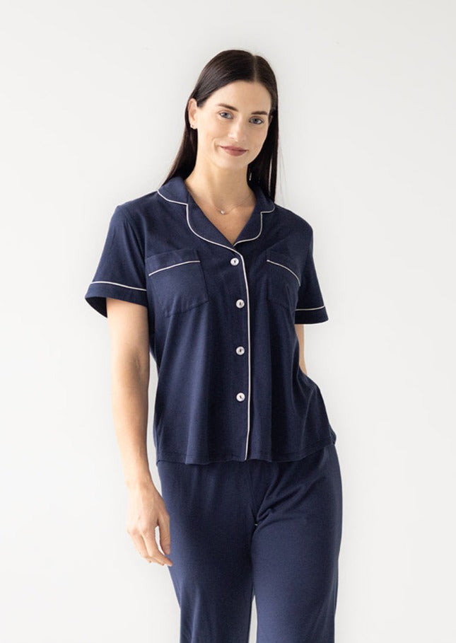 Woman wearing a navy pajama set with white piping on a white background