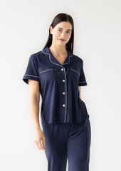 Woman wearing a navy pajama set with white piping on a white background
