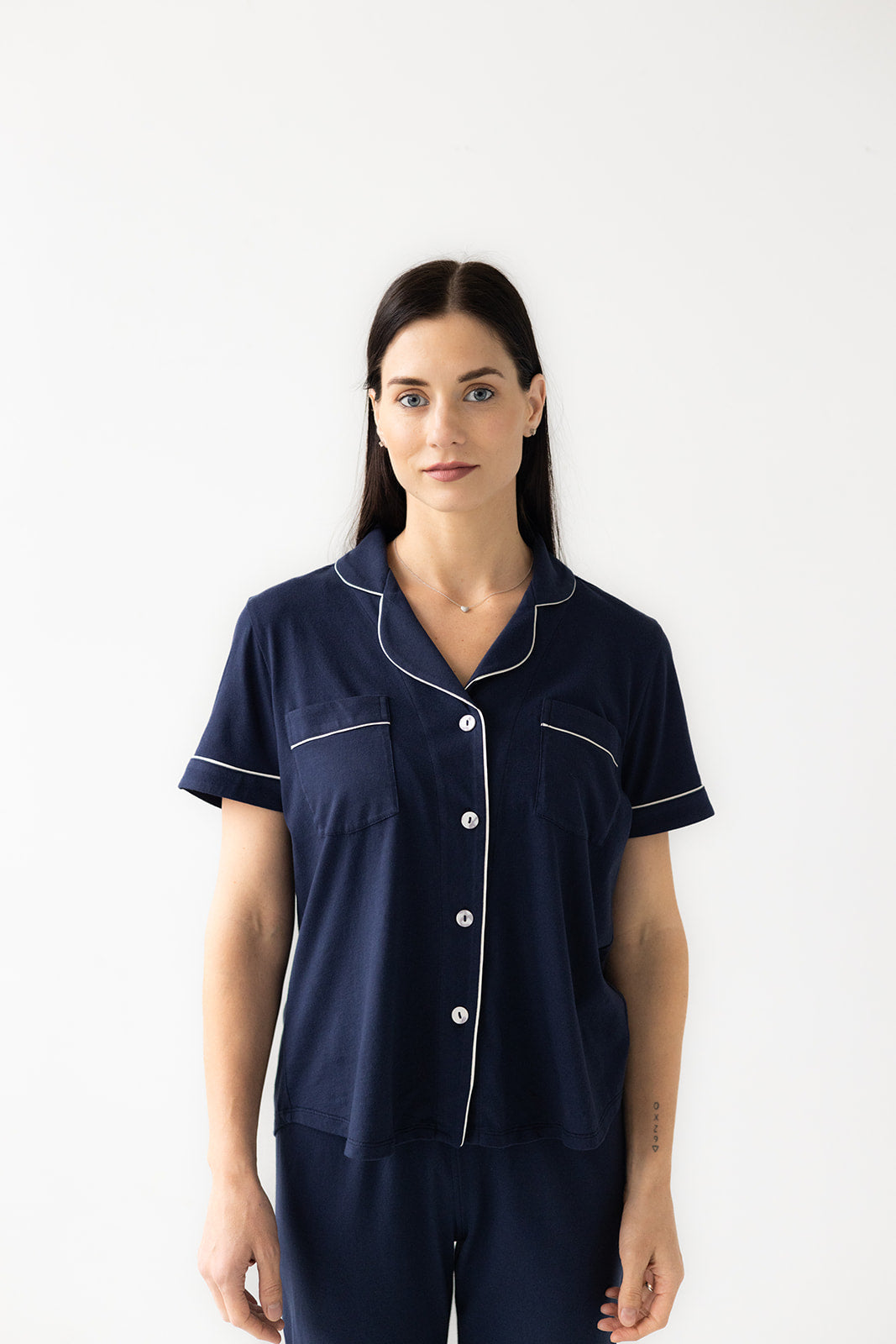 Woman wearing navy blue pajamas with white piping on a white background