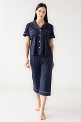 Woman wearing navy blue pajama set with white trim on a white background