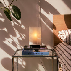 Glass nightstand with books and a lamp next to a bed with striped bedding.