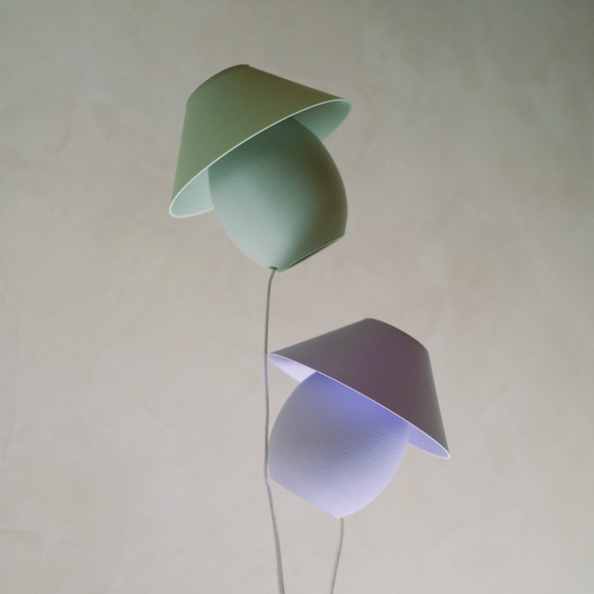 Two modern pendant lights, one green and one purple, on a plain background.