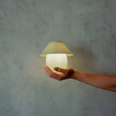 Hand holding a glowing spherical lamp against a textured gray background