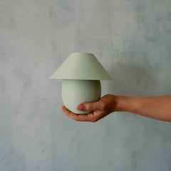 Hand holding a small green lamp against a gray background