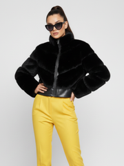 Woman wearing a black faux fur jacket and yellow pants on a white background