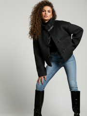 Woman wearing a black coat, blue jeans, and black knee-high boots on a gray background